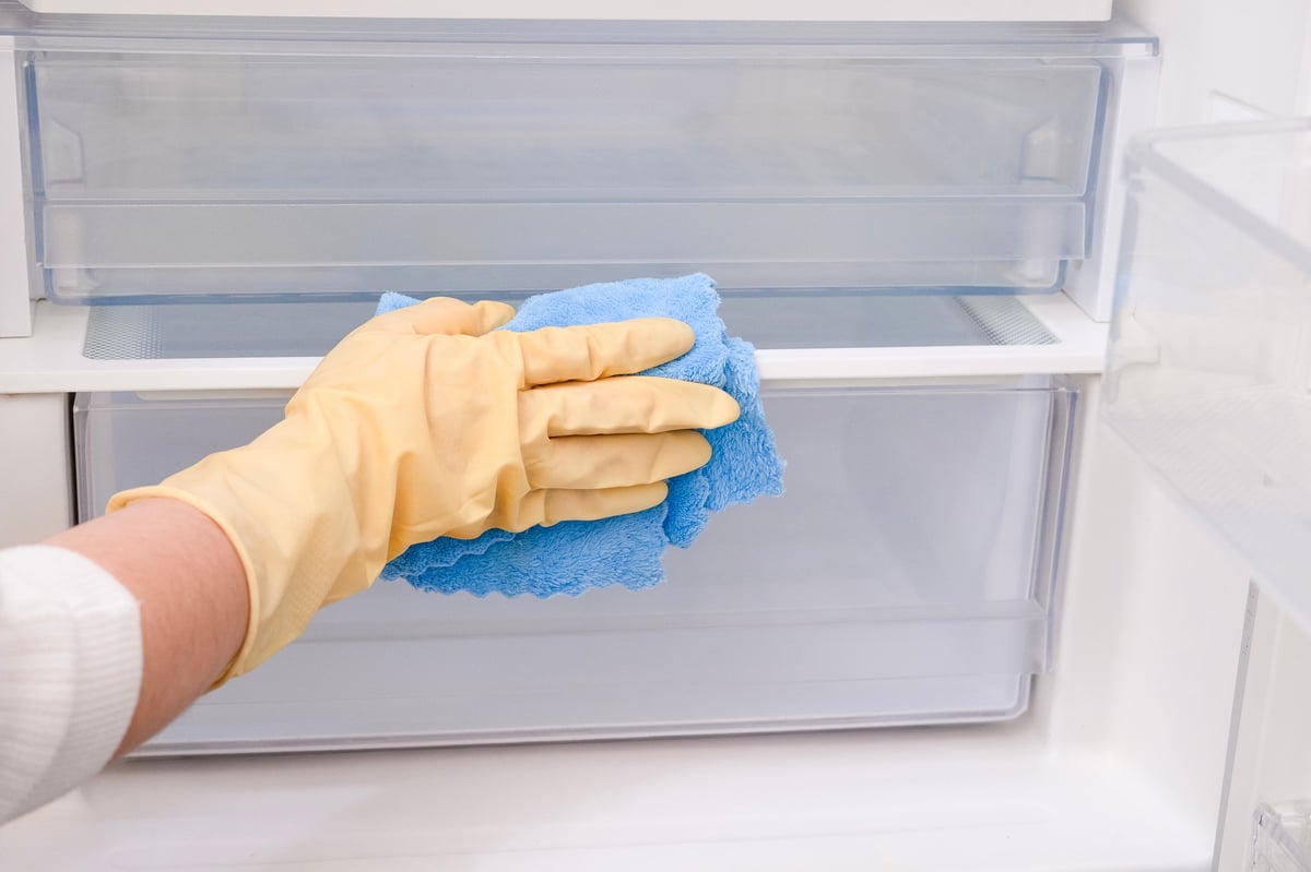 Close-up of a woman's gloved hand wiping down a refrigerator with eco-friendly products